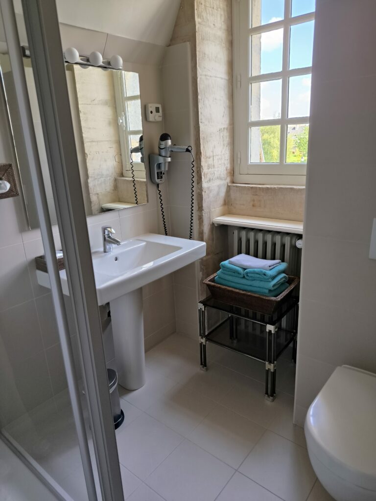 Modern bathroom equipped with a sink, a shower, and towels, with stone and window walls letting light enter.