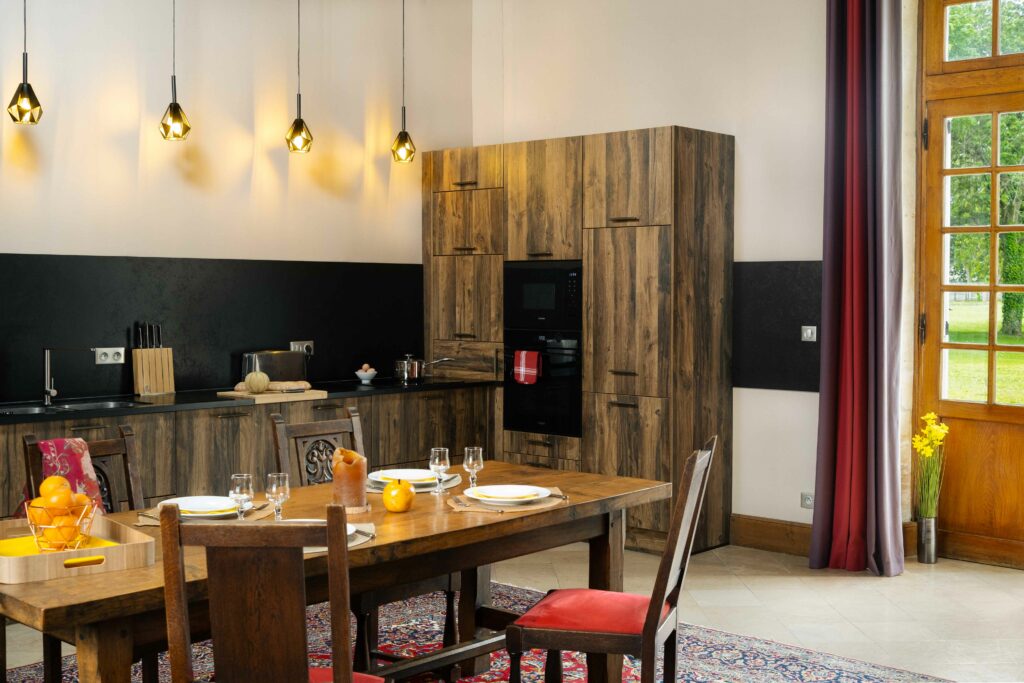 Cucina calda e moderna della grande fattoria Crépon, con tavolo in legno, arredamento autentico e luce naturale.