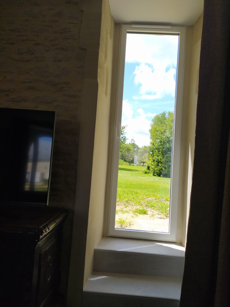 Utsikt över ett fönster från Le Cerisier Cottage, med utsikt över en grön park och en solig himmel.