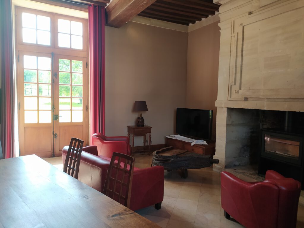 Varm inre av Le Colimçon Gîte, med röda fåtöljer, ett stort fönster och en trevlig lounge.