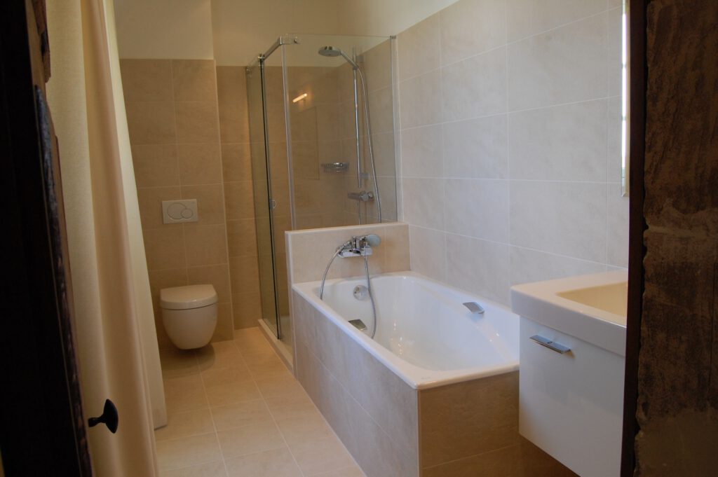 Modernt badrum med badkar, walk -in dusch och wc, med lätta kaklade väggar i ett logi i Normandie.