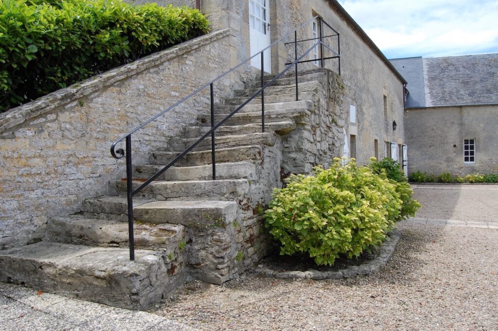 Sten trappa som leder till Le Poirier Cottage, omgiven av grönska, inom Grande Ferme de Crépon i Normandie.