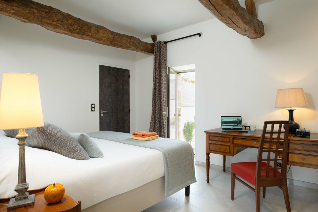 Camera comoda con letto matrimoniale, scrivania in legno, lampade di illuminazione e accesso esterno in un ambiente storico.